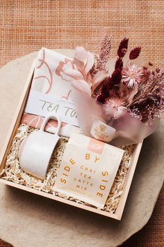 an open box containing a coffee mug, tea bag and flowers