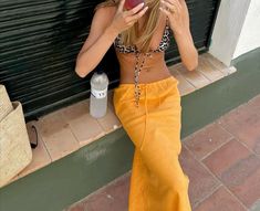 a woman sitting on the side of a building while holding an apple in her hand