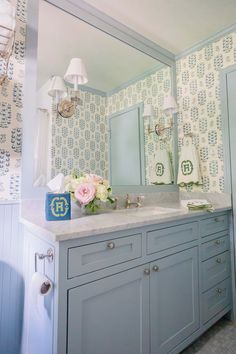 a bathroom with blue and white wallpaper has a large mirror above the double sink