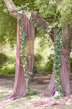 an outdoor wedding ceremony with pink drapes and greenery draped around the tree branches