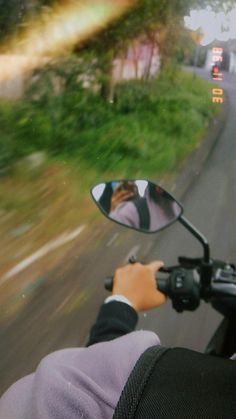 a person on a motorcycle taking a selfie in the side mirror while riding down the road