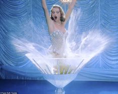 a woman in a white dress standing on top of a glass vase with feathers flying around her