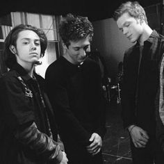 three young men standing next to each other in front of a microphone and recording equipment