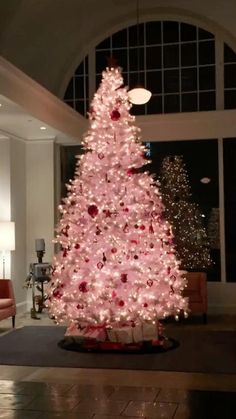 a pink christmas tree is in the middle of a room with large windows and lights