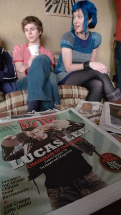 two people sitting on a couch in front of some magazine covers and coffee mugs