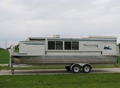 a trailer with a boat on the back is parked in front of a green field