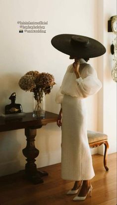 a woman with a black hat on her head is standing in front of a table