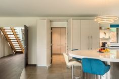 a kitchen with white counter tops and blue stools next to a spiral stair case