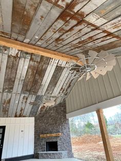 an empty room with a ceiling fan and brick fireplace in the center, surrounded by wood planks