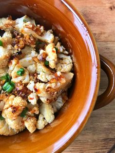 a brown bowl filled with cauliflower on top of a wooden table