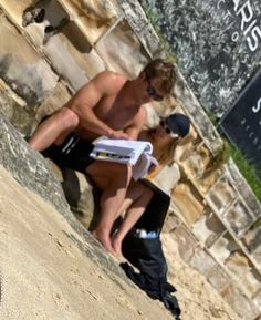 a shirtless man sitting on the side of a stone wall next to a woman