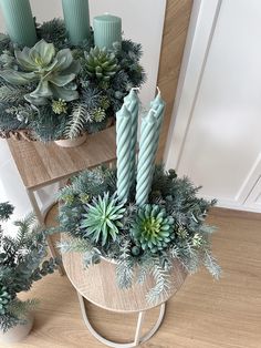 two candles are sitting on a table with succulents and other greenery