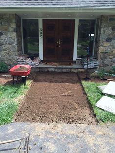 a red wheelbarrow is sitting in front of a house with gravel and grass