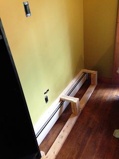 a room with yellow walls and wooden flooring in the corner, there is a small bench next to it