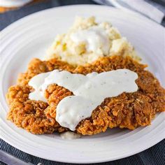 two fried chicken patties covered in gravy on a plate with mashed potatoes