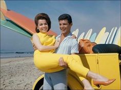 a man and woman sitting on the back of a yellow car with surfboards behind them