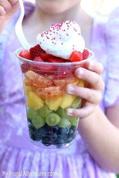 a person holding up a plastic cup with fruit in it and the words rainbow fruit cup