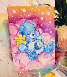 a painting of a blue teddy bear sleeping on a pink cloud with yellow stars in the sky