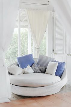 a white round couch with blue and white pillows on it in front of a window