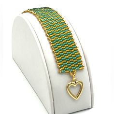 a green and gold beaded bracelet with a heart charm on it's side