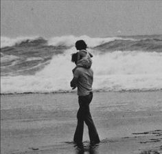 a man carrying a woman on his back while walking along the beach with waves in the background