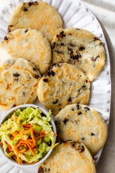 a white plate topped with food next to a bowl of coleslaw and biscuits