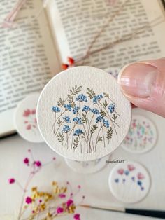 a person holding up a flower sticker on top of a book with flowers around it