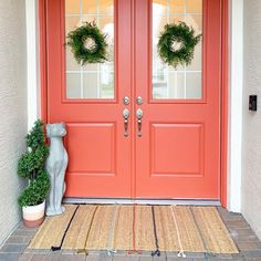 a red door with two wreaths on it and a cat statue next to it