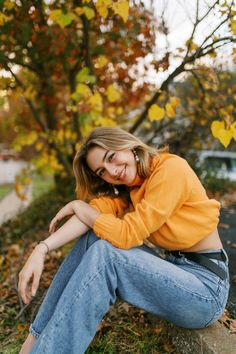 a young woman sitting on the ground in front of trees with leaves all around her