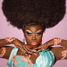 a woman with an afro standing in front of a purple background wearing a blue dress