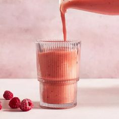 a person is pouring something into a glass with raspberries on the side