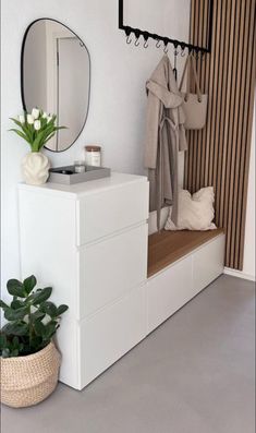 a white dresser sitting under a mirror next to a potted plant and coat rack