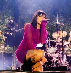 a woman kneeling down on top of a stage next to a microphone and drum set