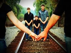 the family is standing on railroad tracks with their hands in each other's palms