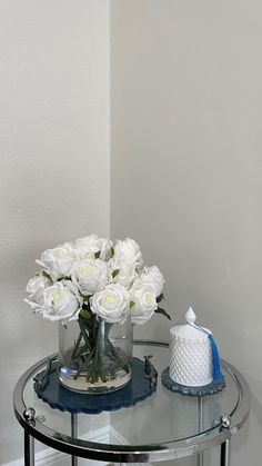 a glass table topped with white flowers and a vase filled with roses on top of it