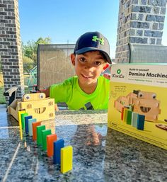 a young boy sitting at a table next to a box of dominos and a book