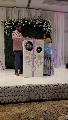 a man standing next to a woman in front of a cake box on top of a stage