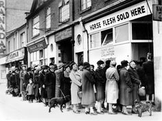 an old black and white photo of people standing in front of a store with their dogs