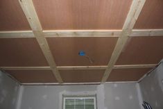 an unfinished room with wood paneling on the ceiling and a window in the corner