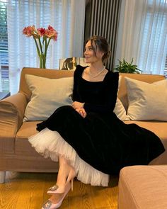 a woman in a black dress sitting on a couch