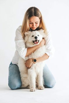 a woman sitting on the floor holding a white dog in her arms and smiling at the camera