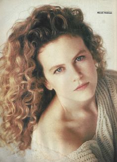 a woman with curly hair is looking at the camera while wearing a sweater and posing for a photo