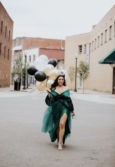 a woman is walking down the street with balloons in her hand and wearing a green dress