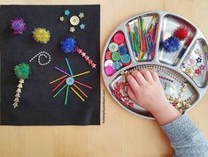 a child's hand is on the tray next to some crafting supplies that include buttons and pins