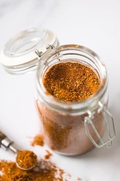 a jar filled with spices sitting on top of a white counter next to a spoon