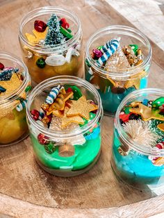 four glass jars filled with different types of christmas treats on a wooden tray and decorated with ornaments