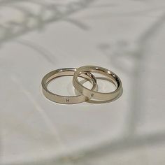 two silver wedding rings sitting on top of a white surface with tree branches in the background