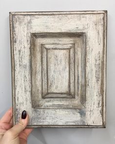 a person holding up an old white frame with a square in the middle and black nail polish on it