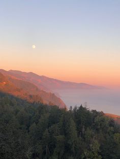 the sun is setting over some mountains with trees on each side and fog in the air