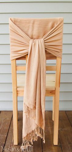 a wooden chair with a tan scarf draped over it's back on a wood floor